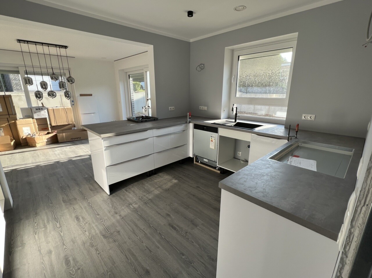 Modern kitchen under construction: white cabinets, gray countertops, sink, dishwasher, boxes