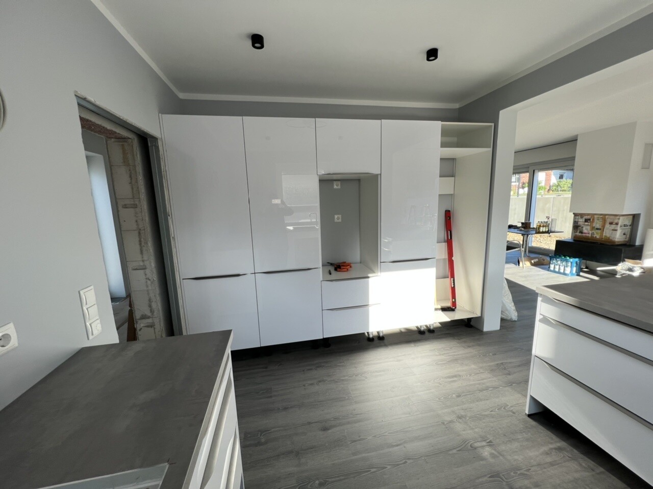 Modern kitchen with white high-gloss cabinets, refrigerator niche, and red spirit level.