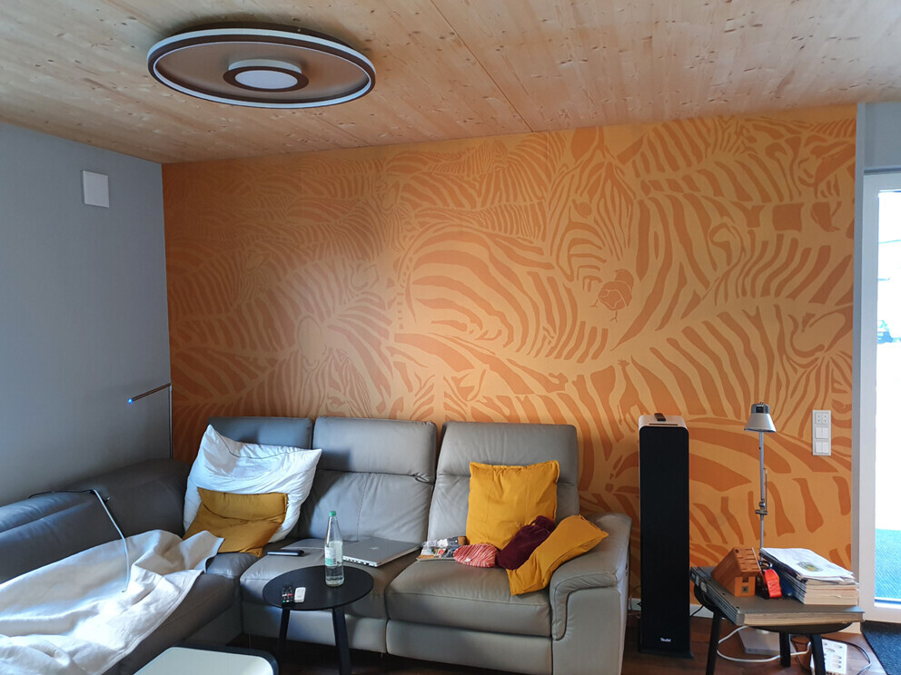 Living room with gray leather sofa in front of orange zebra-striped wall; yellow cushions, coffee table, speakers.