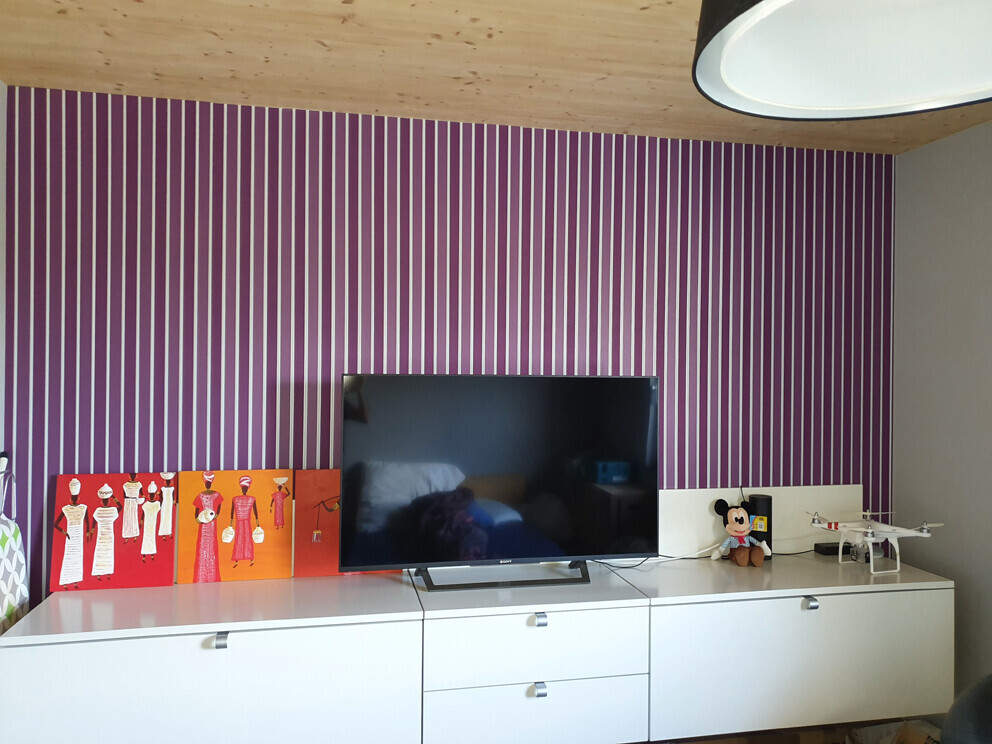 TV on white sideboard in front of purple striped wall; Mickey Mouse plush toy and drone beside it.
