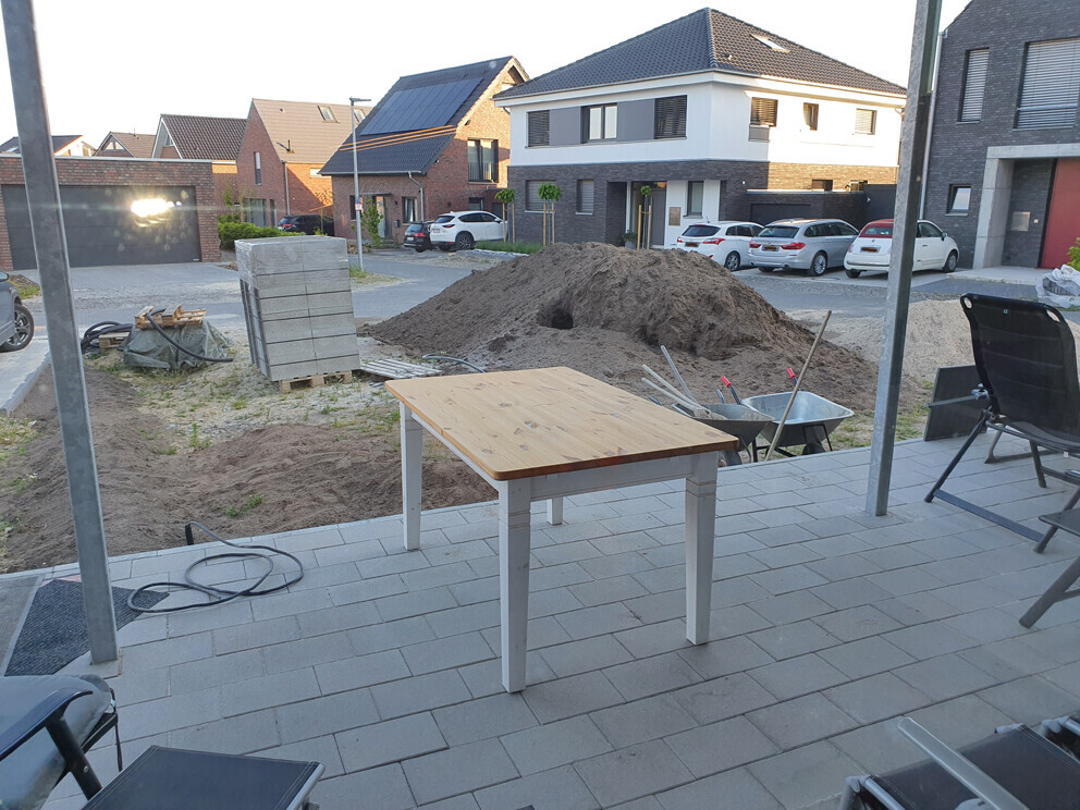 Construction site in residential area: wooden table on terrace, soil piles, building materials, wheelbarrow.