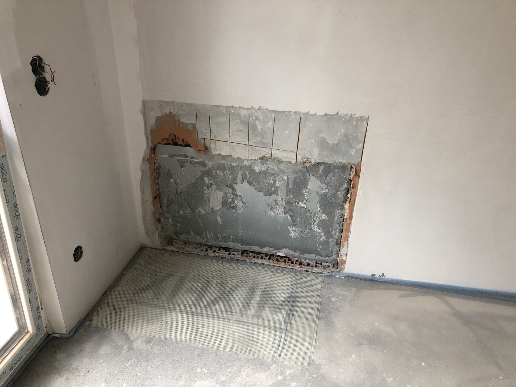 Raum mit freigelegter Wandfläche: ausgebrochene Mauer, Fliesenreste und offenes Kabelwerk.