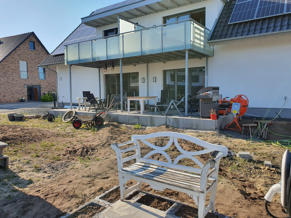 Modern white single-family house with balcony; garden under construction, white garden bench in the foreground.
