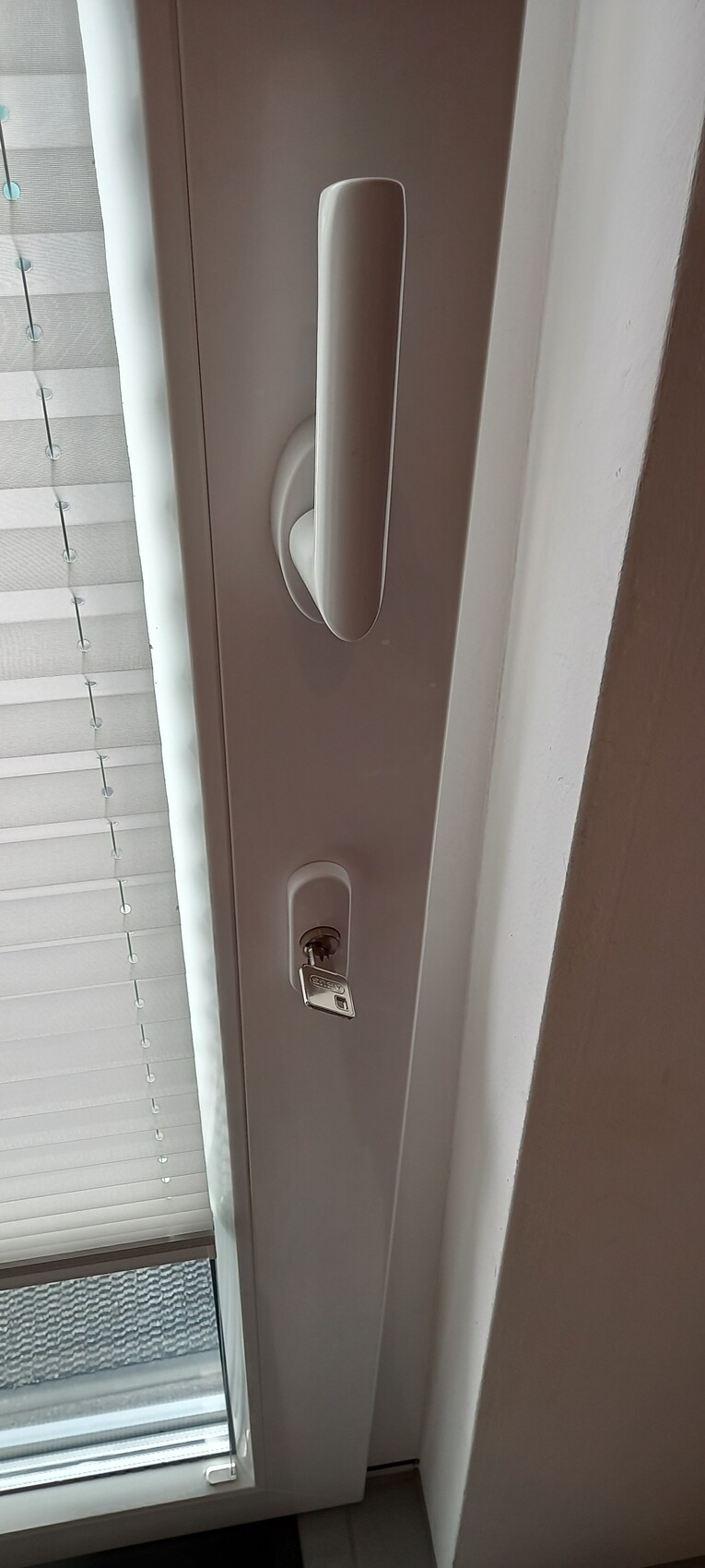 Door with long vertical handle and key in the lock next to a window with venetian blinds.