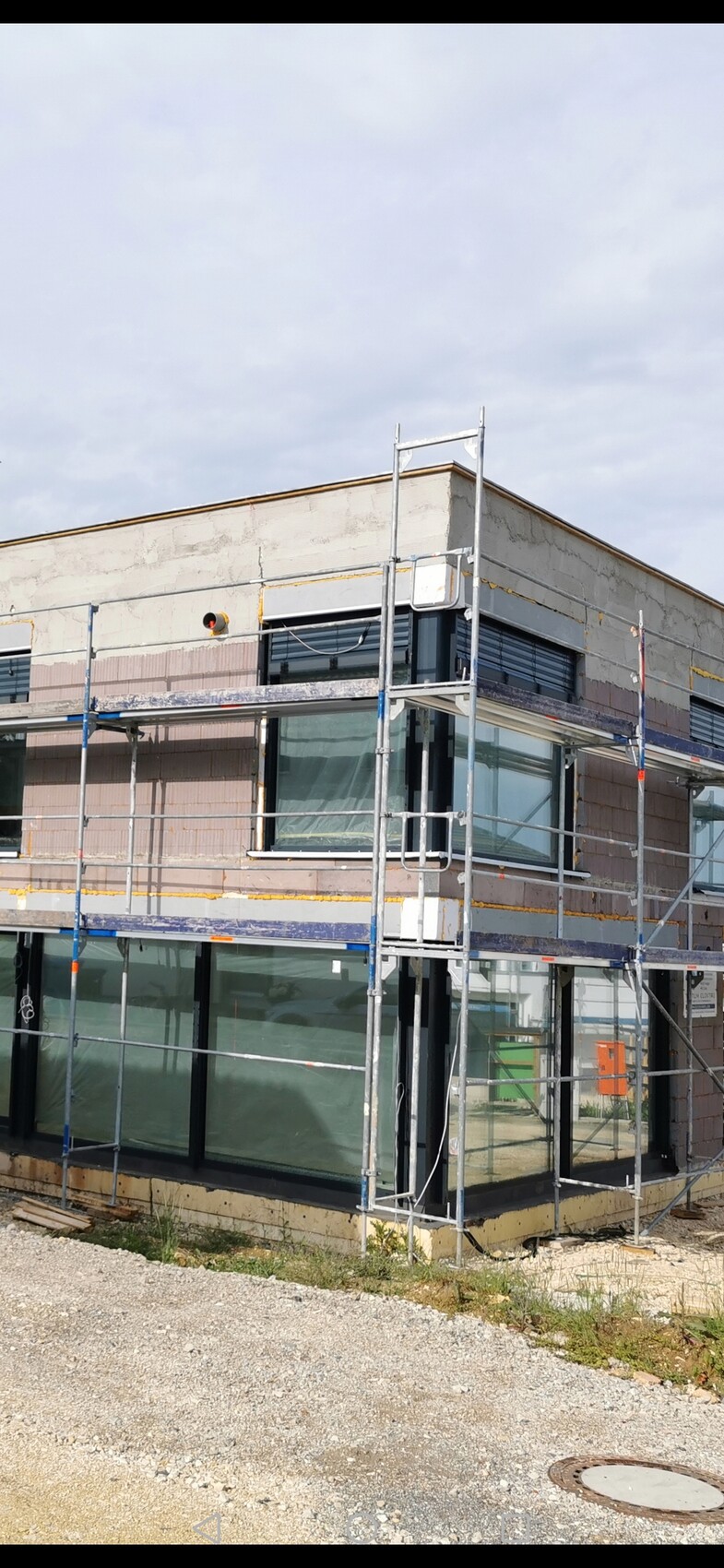 Scaffolding around a modern commercial building with large glass windows, incomplete exterior facade.