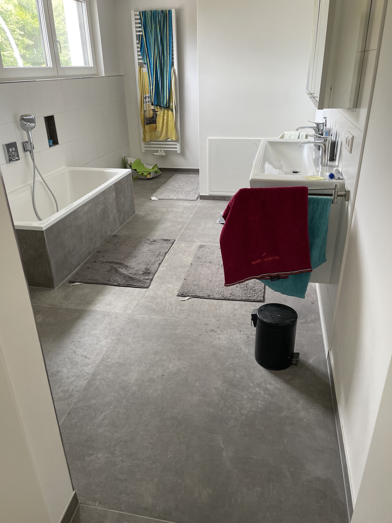 Helles Badezimmer: Badewanne links, Waschbecken rechts, bunte Handtücher am Heizkörper.