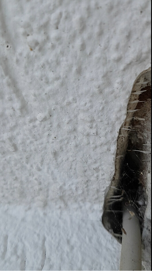 Close-up of a white, rough wall with a hole showing a visible pipe.