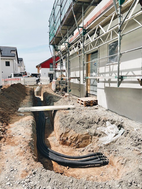 Excavation pit with black pipes next to building, wooden bridge over pit, scaffolding