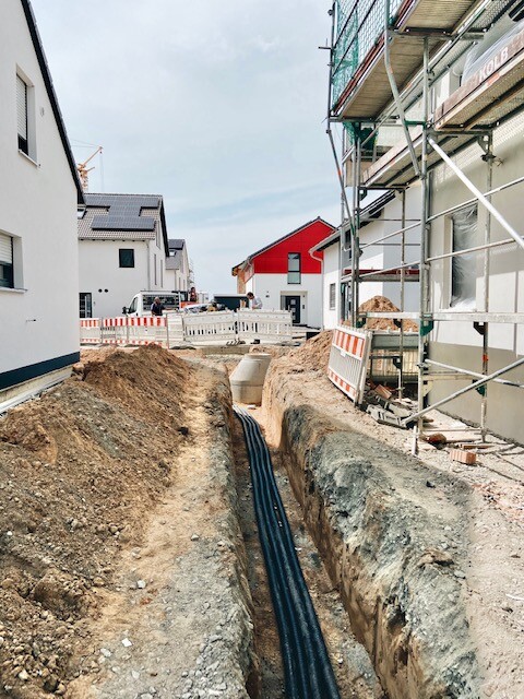 Construction site: excavation pit with black pipes, barriers, scaffolding on buildings.