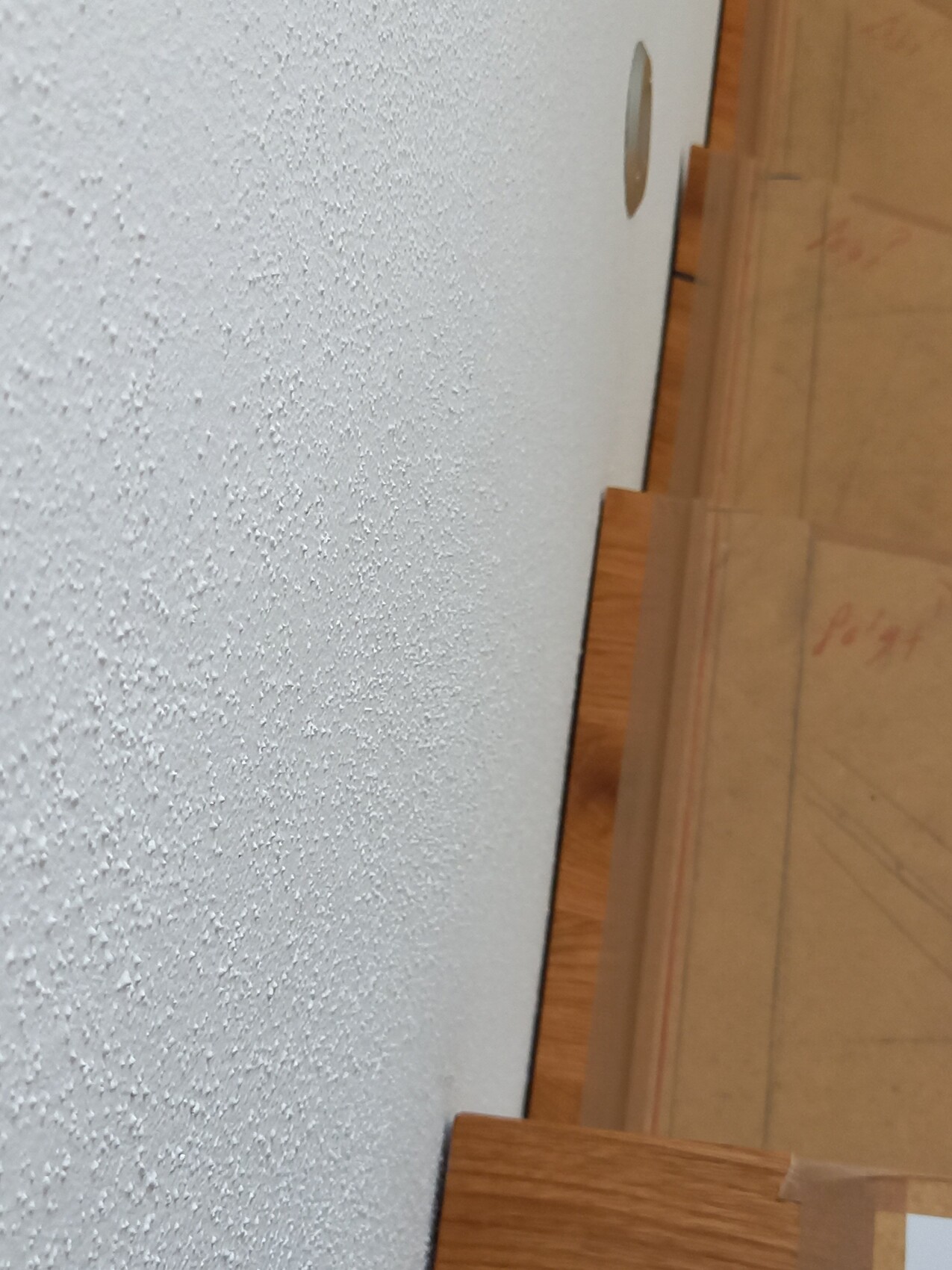 White, coarse-textured wall next to a wooden staircase; hole in the wall.