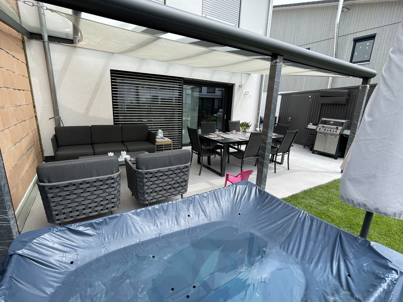 Garten-Terrasse mit schwarzer Lounge-Sitzgruppe, Esstisch, Grill, Pool unter Pergola.