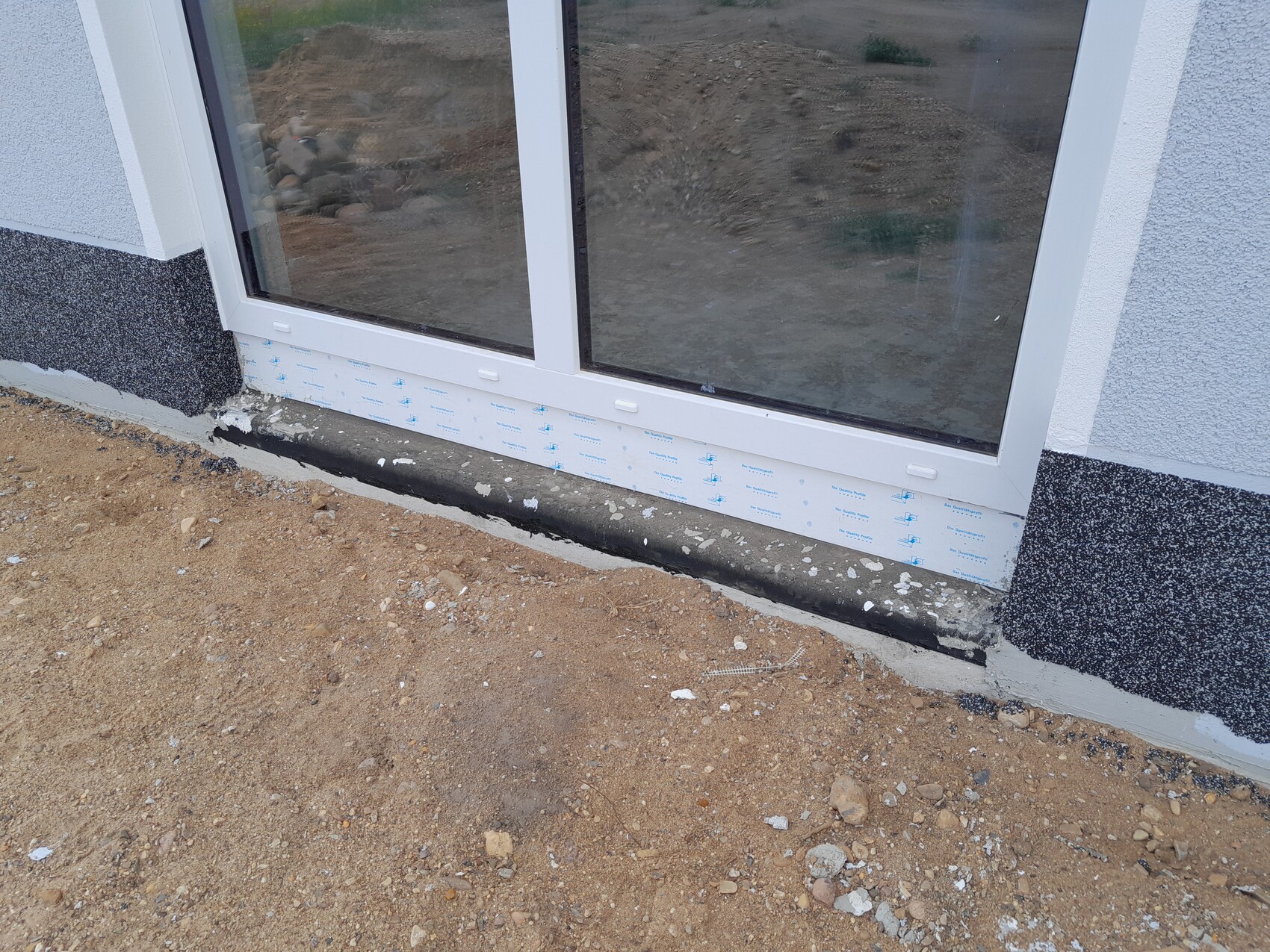 White sliding glass door in the wall opening; construction site floor made of soil and gravel in front.