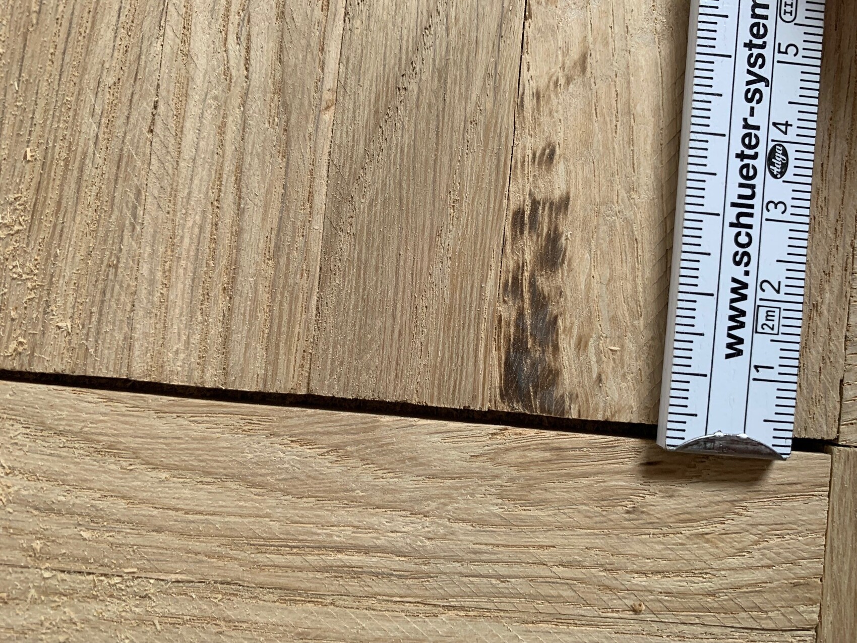 Close-up of wooden boards with coarse wood grain; to the right, a tape measure with centimeter markings.
