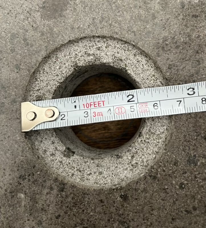 Round hole in concrete floor with measuring tape laid across to measure diameter