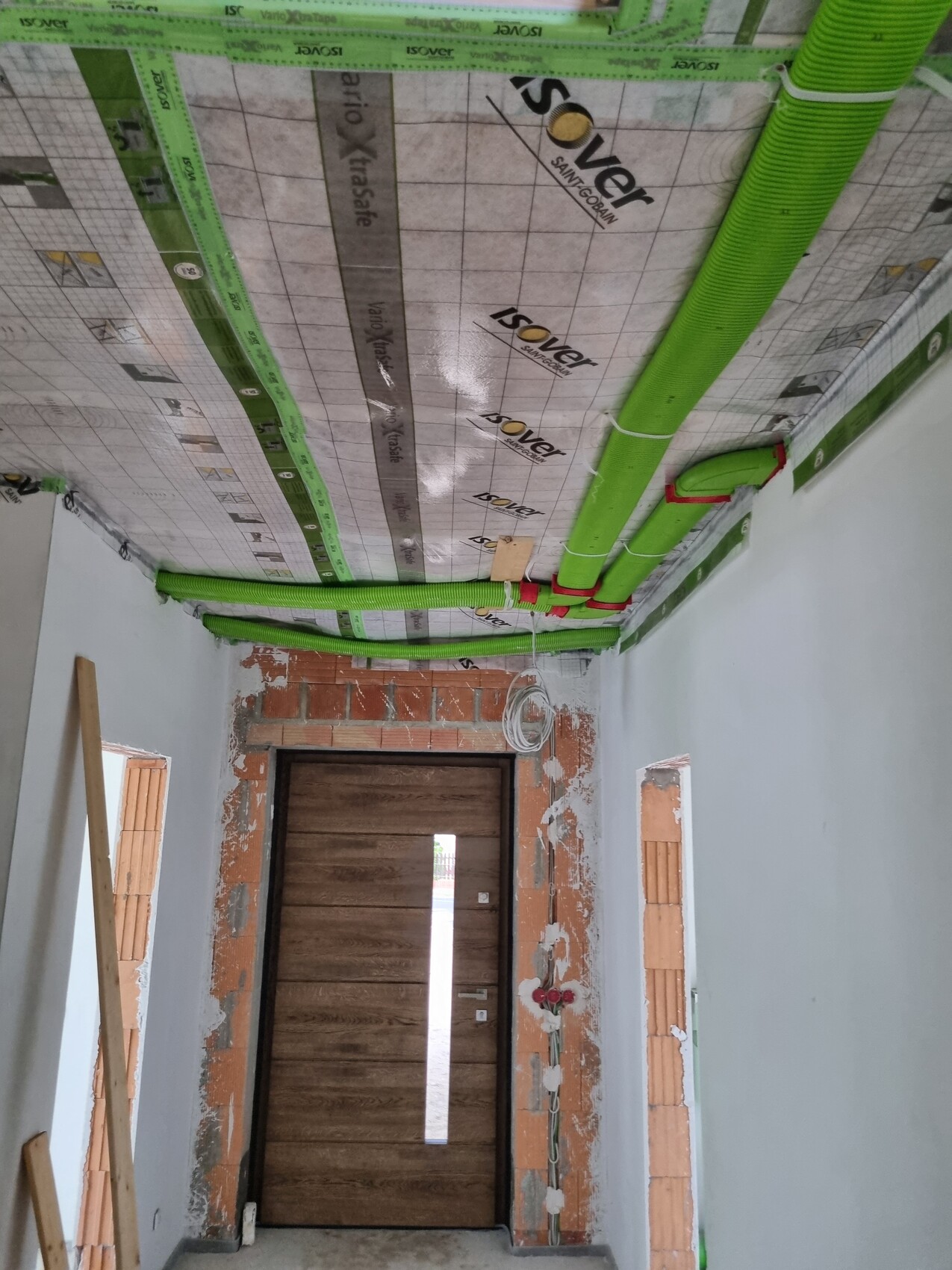 Baustelle Innen: grüne Installationsrohre an der Decke, Dämmung, Tür am Ende.