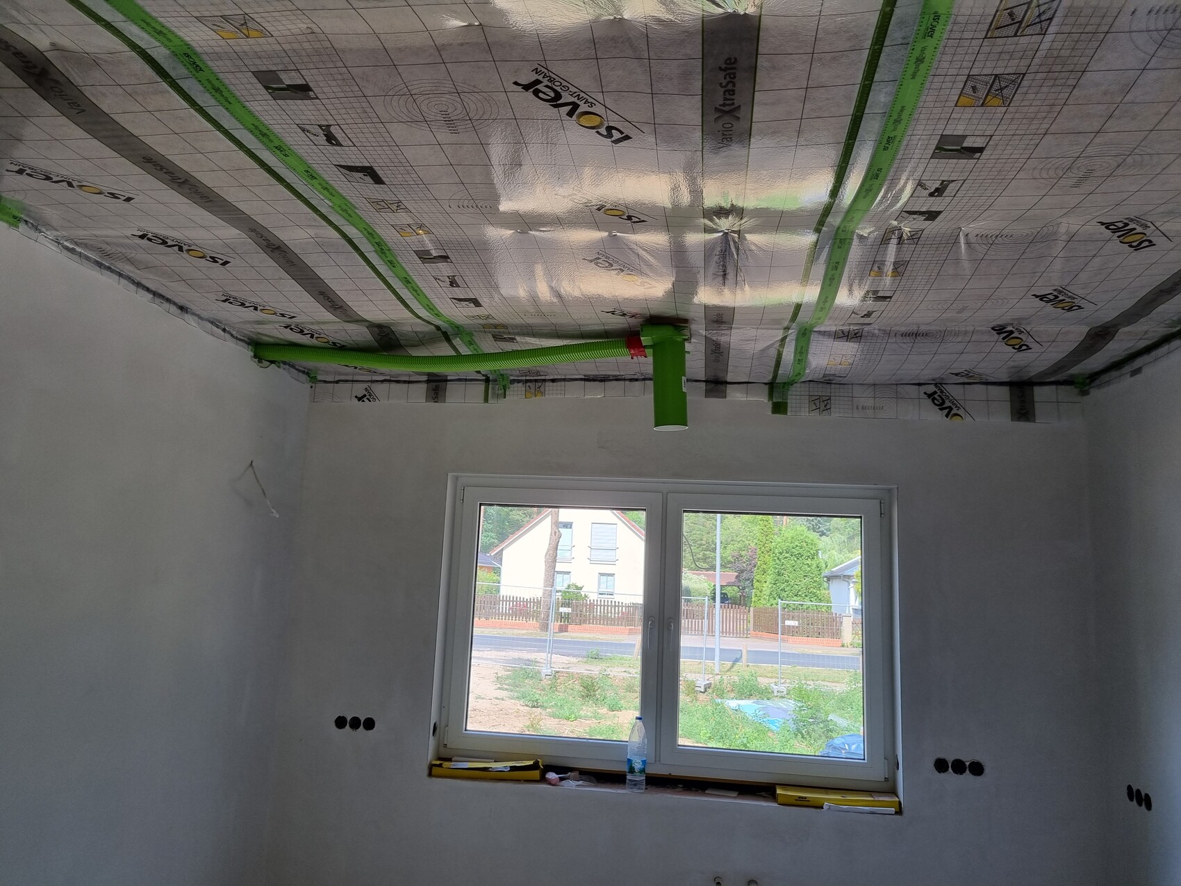 Renoviertes Zimmer mit Dämmfolie an der Decke, grünen Rohren, Fensterfront und Blick nach außen.