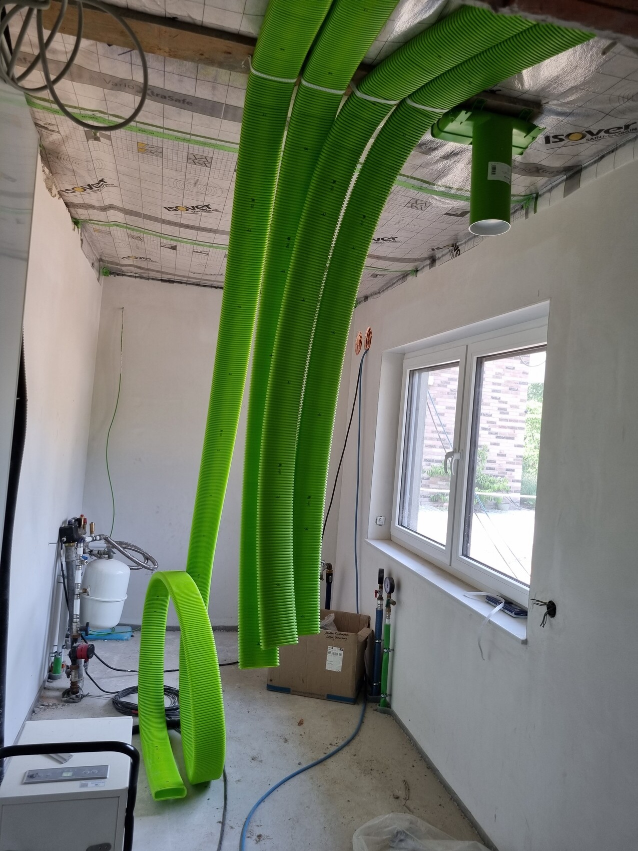 Grüne flexible Lüftungsrohre hängen von der Decke in einem Bau-/Installationsraum; Fenster sichtbar