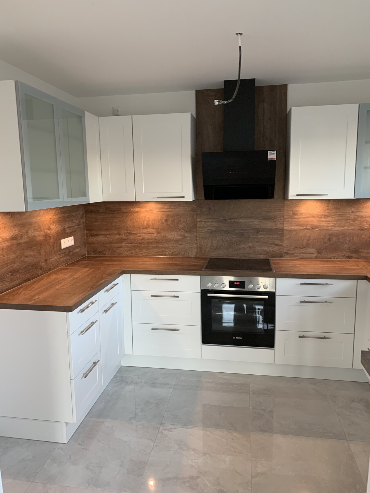 Moderne L-Küche: weiße Oberschränke, Holz-Arbeitsplatten, Bosch-Backofen, schwarzer Dunstabzug.