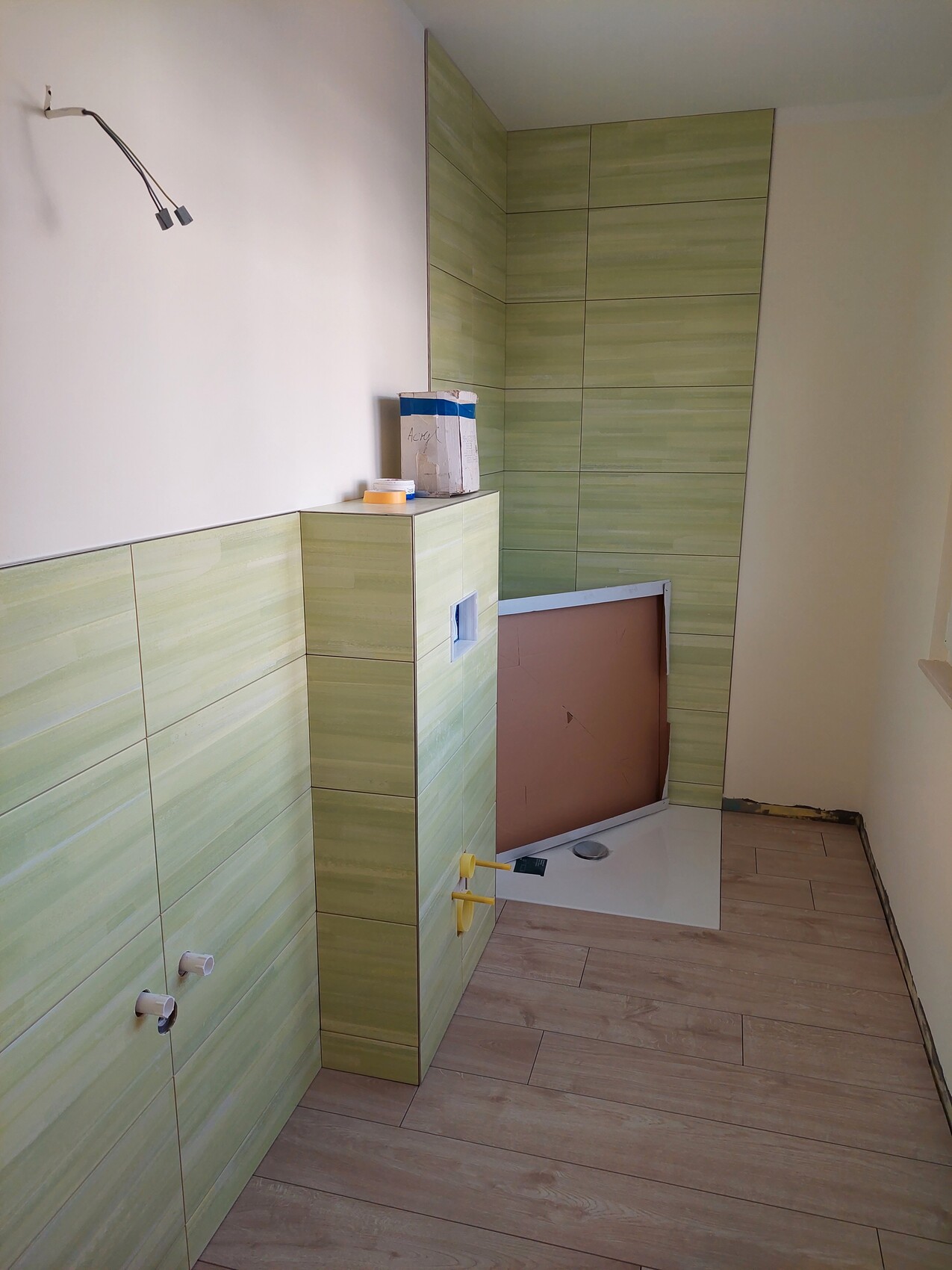 Partially renovated bathroom with green wall and floor tiles, unfinished shower area