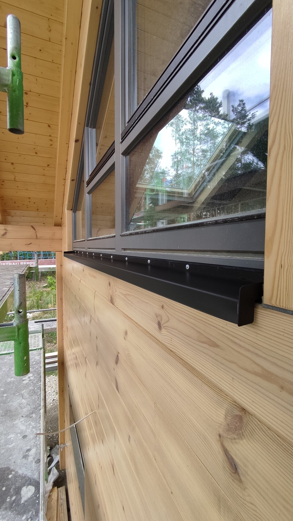 Außenaufnahme eines Holzhauses mit schwarzen Fensterrahmen und Fensterbank; Baugerüst sichtbar.