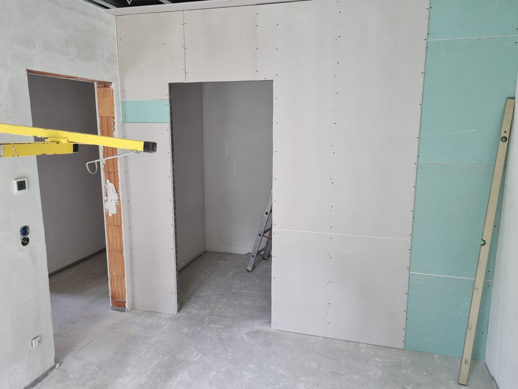 Construction site: Interior with drywall sheets, open passage, ladder, and construction tools.