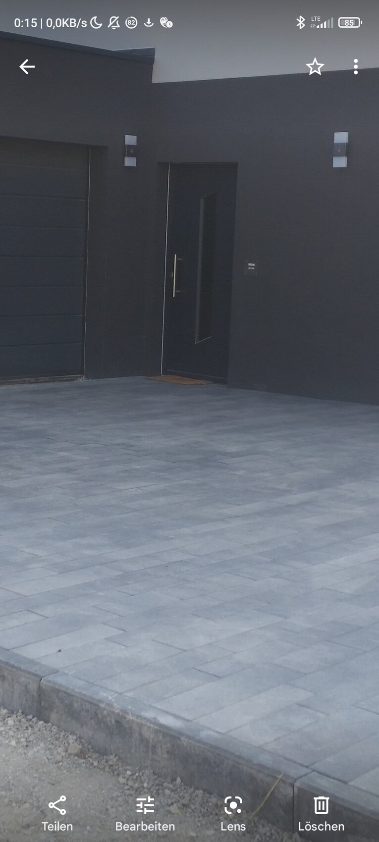 Modern black house facade with dark entrance door next to a garage door; paved courtyard