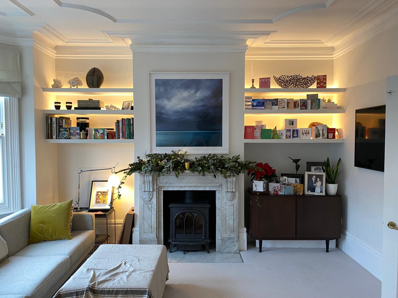 Cozy living room with fireplace, illuminated shelves, pictures and plants