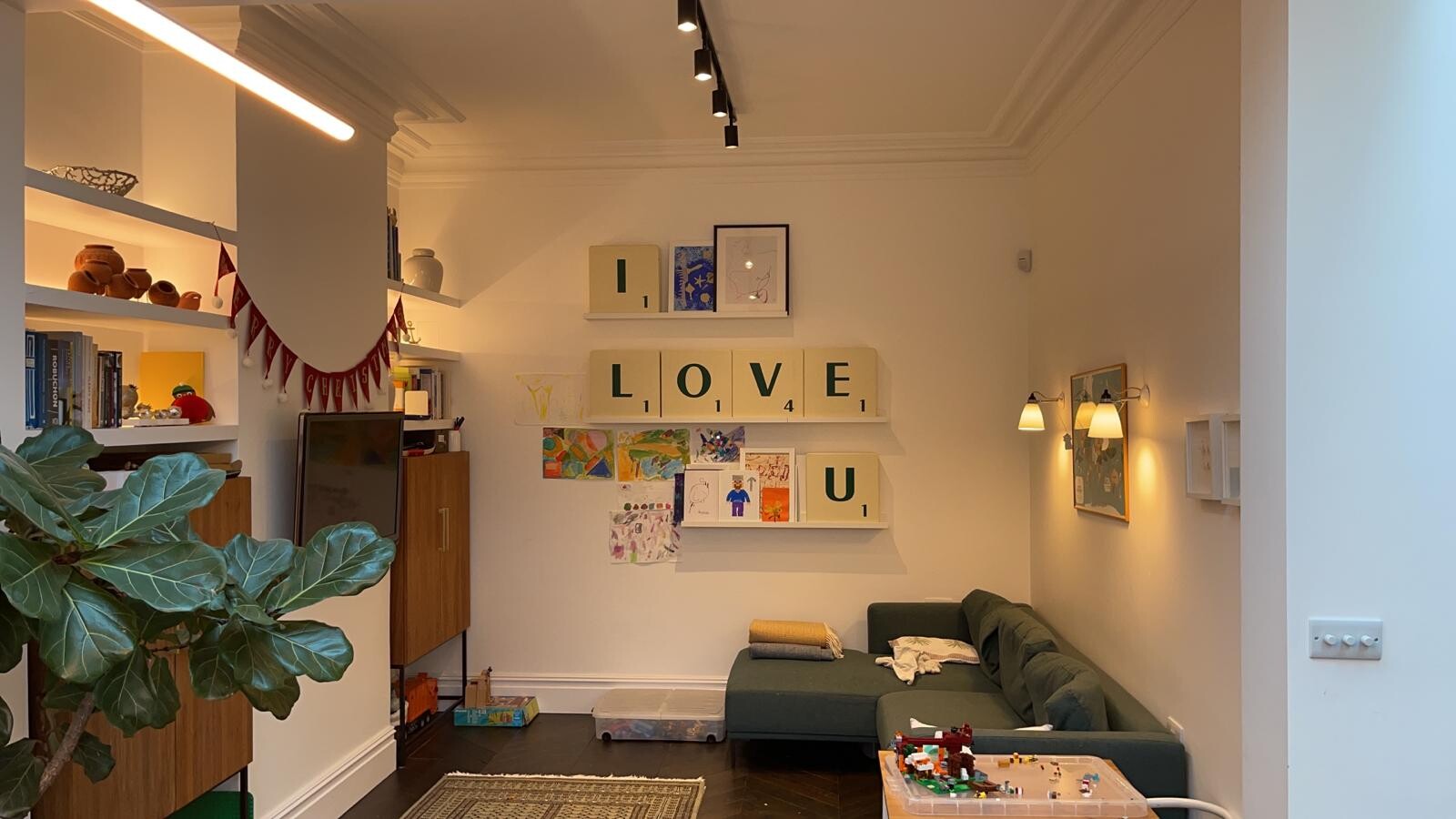 Living room with green corner sofa, bookshelves, children's drawings and letters 'LOVE U' on the wall