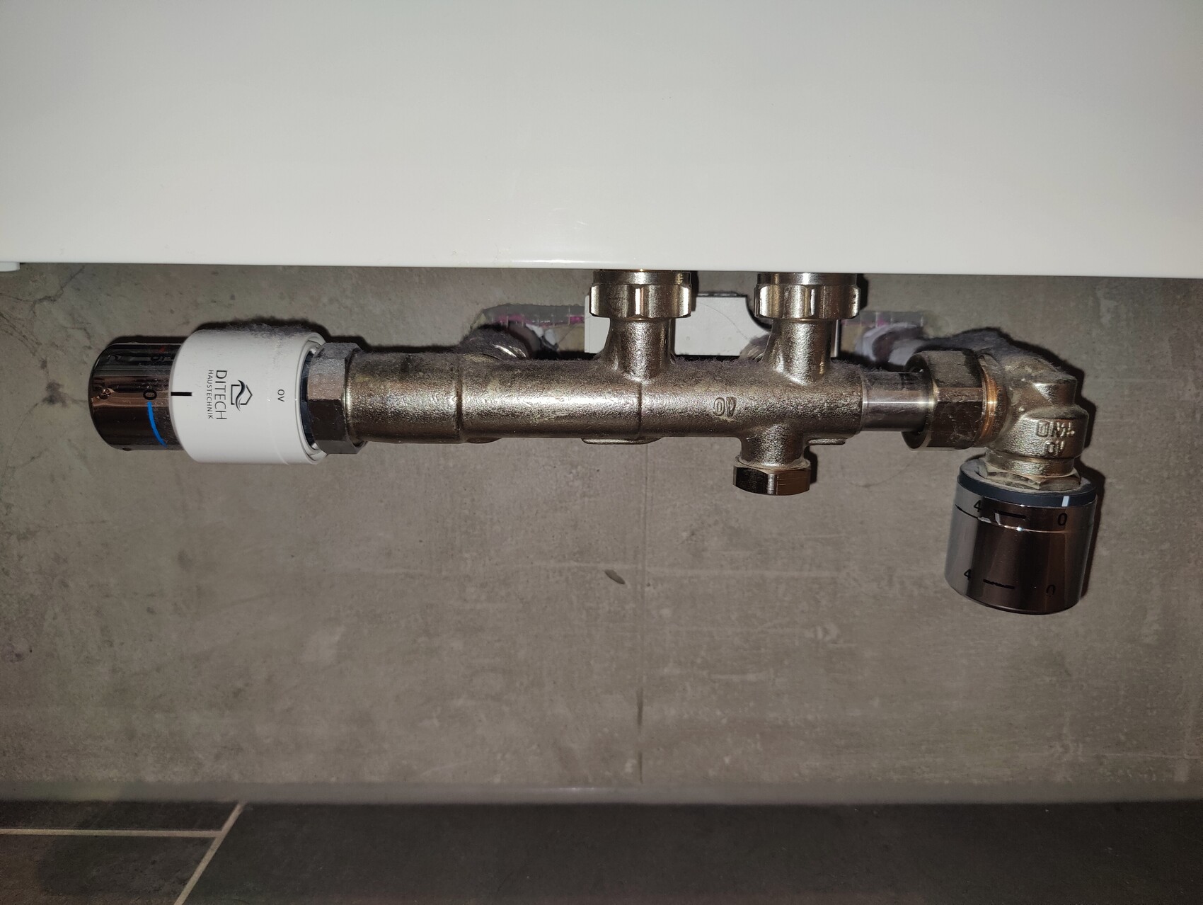 Undersink fitting with filter on the left, central pipe, and adjustable shut-off valve on the right.