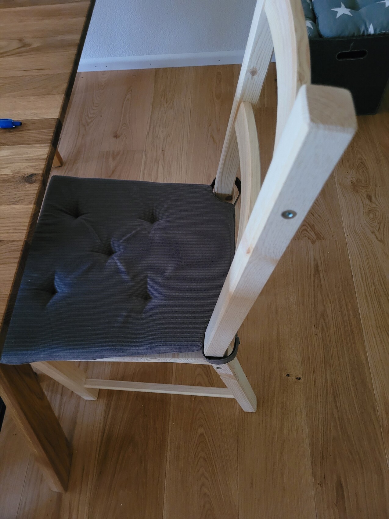Wooden chair with dark gray cushioned seat on light wooden floor.