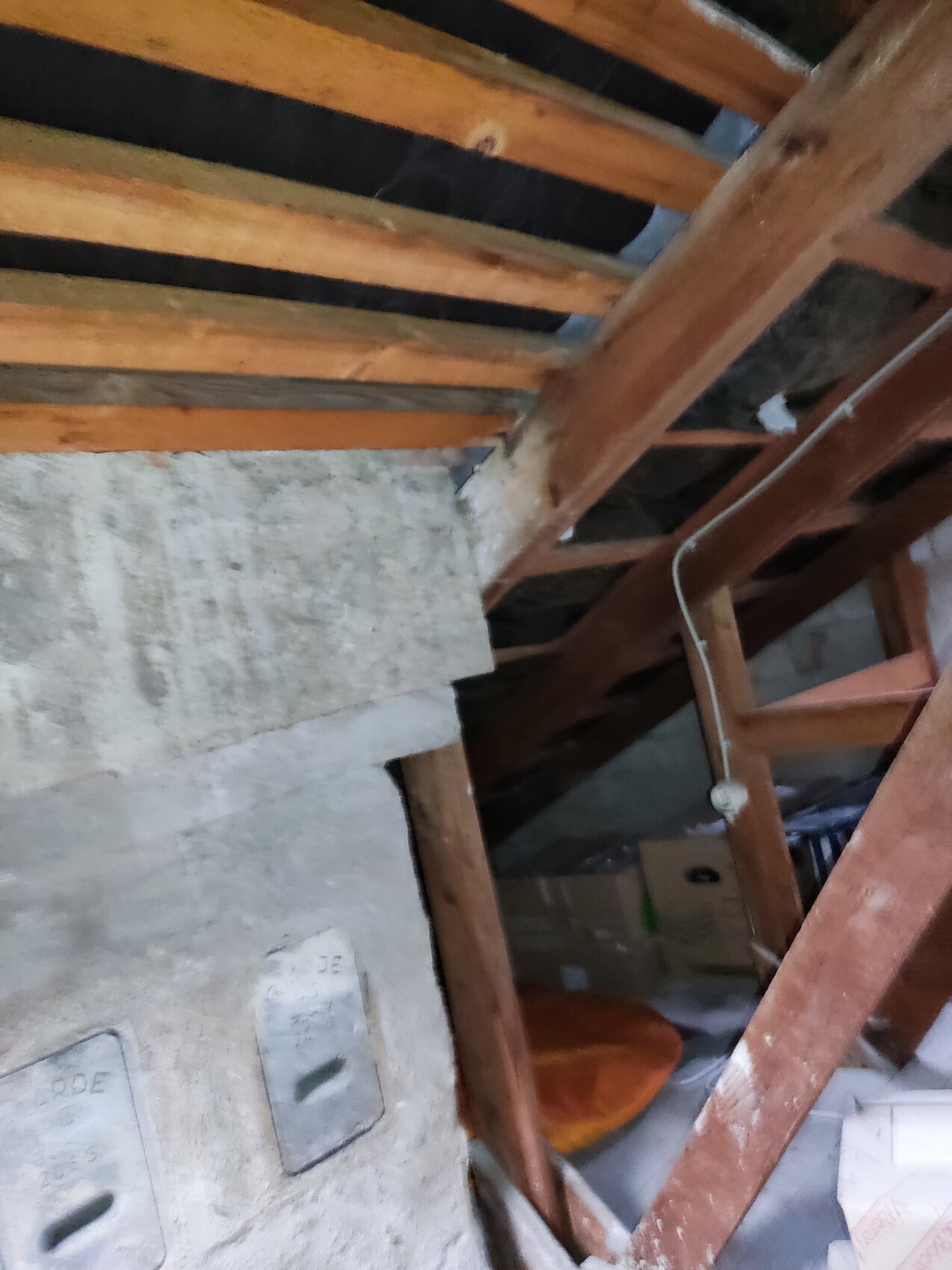 Attic with visible wooden beams, concrete wall, cables, and boxes.