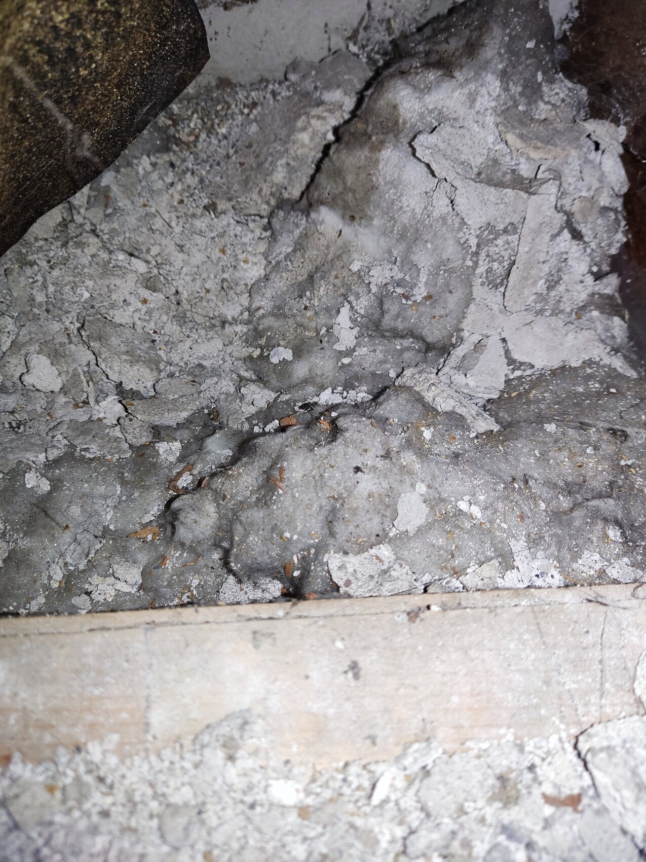 Crumbly concrete and mortar debris with dust, wooden strip at the bottom.