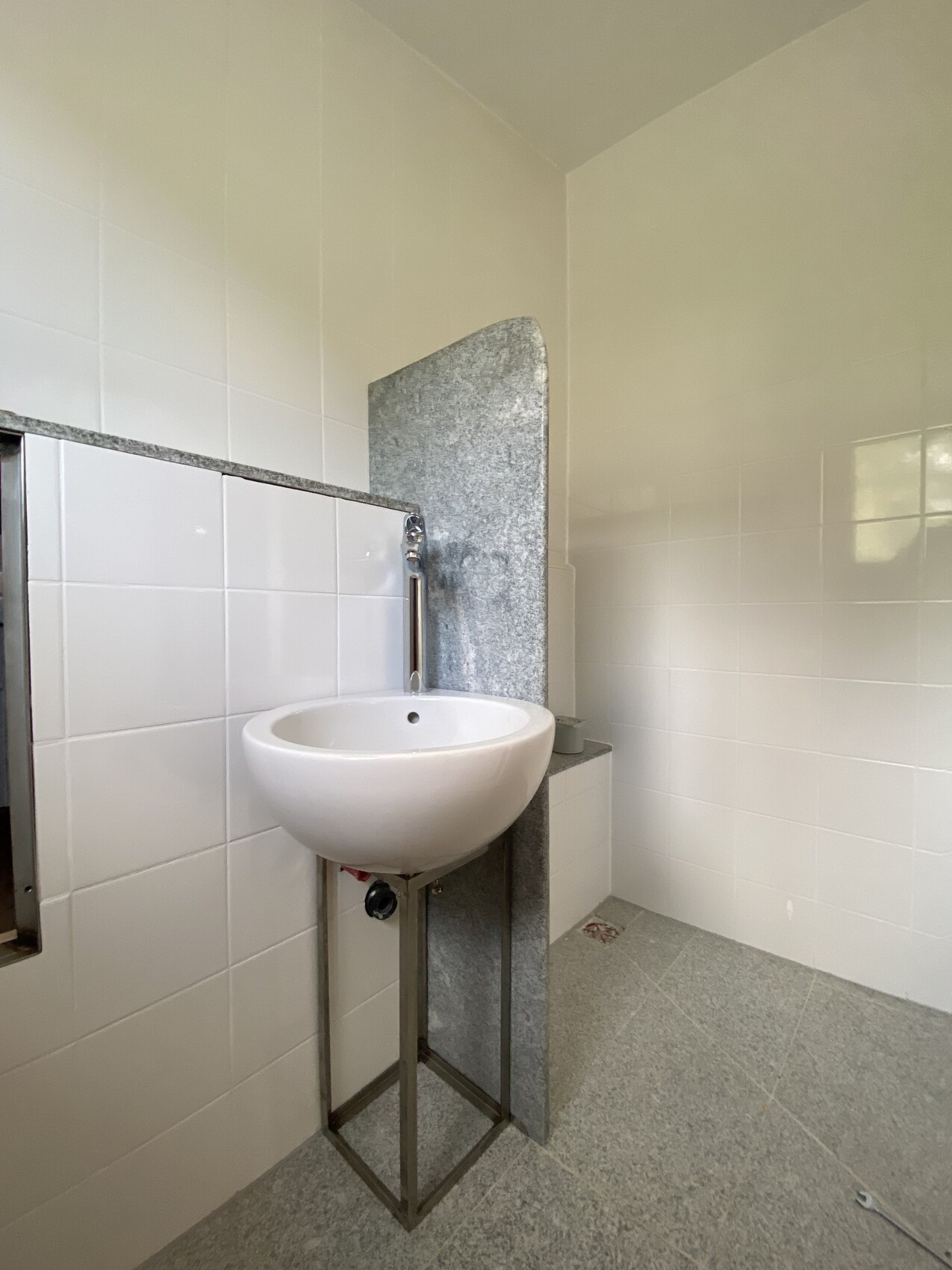 White round washbasin on metal frame in front of grey granite wall in bathroom.