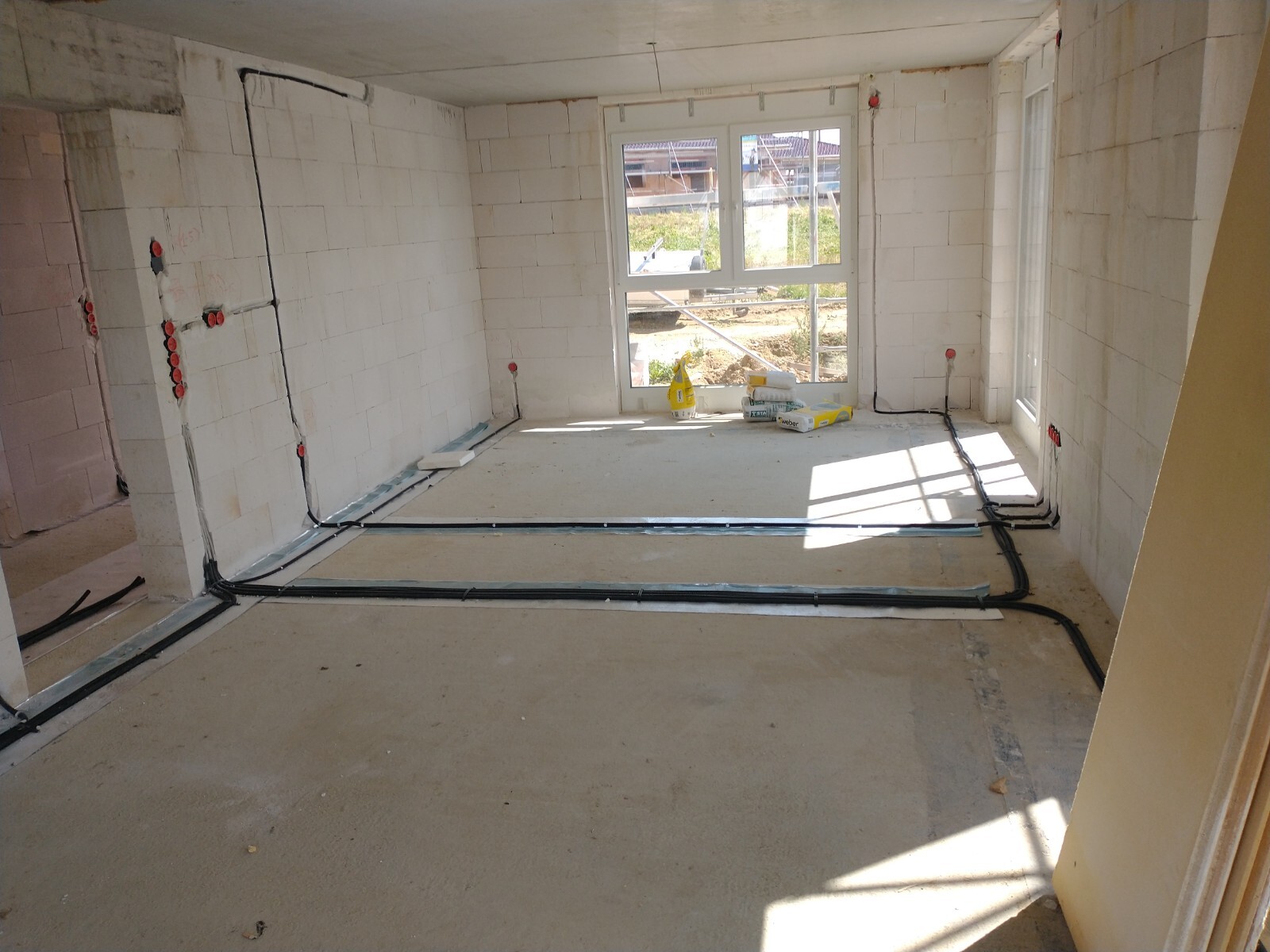 Unfinished construction space with exposed cables on the floor, concrete walls, window front