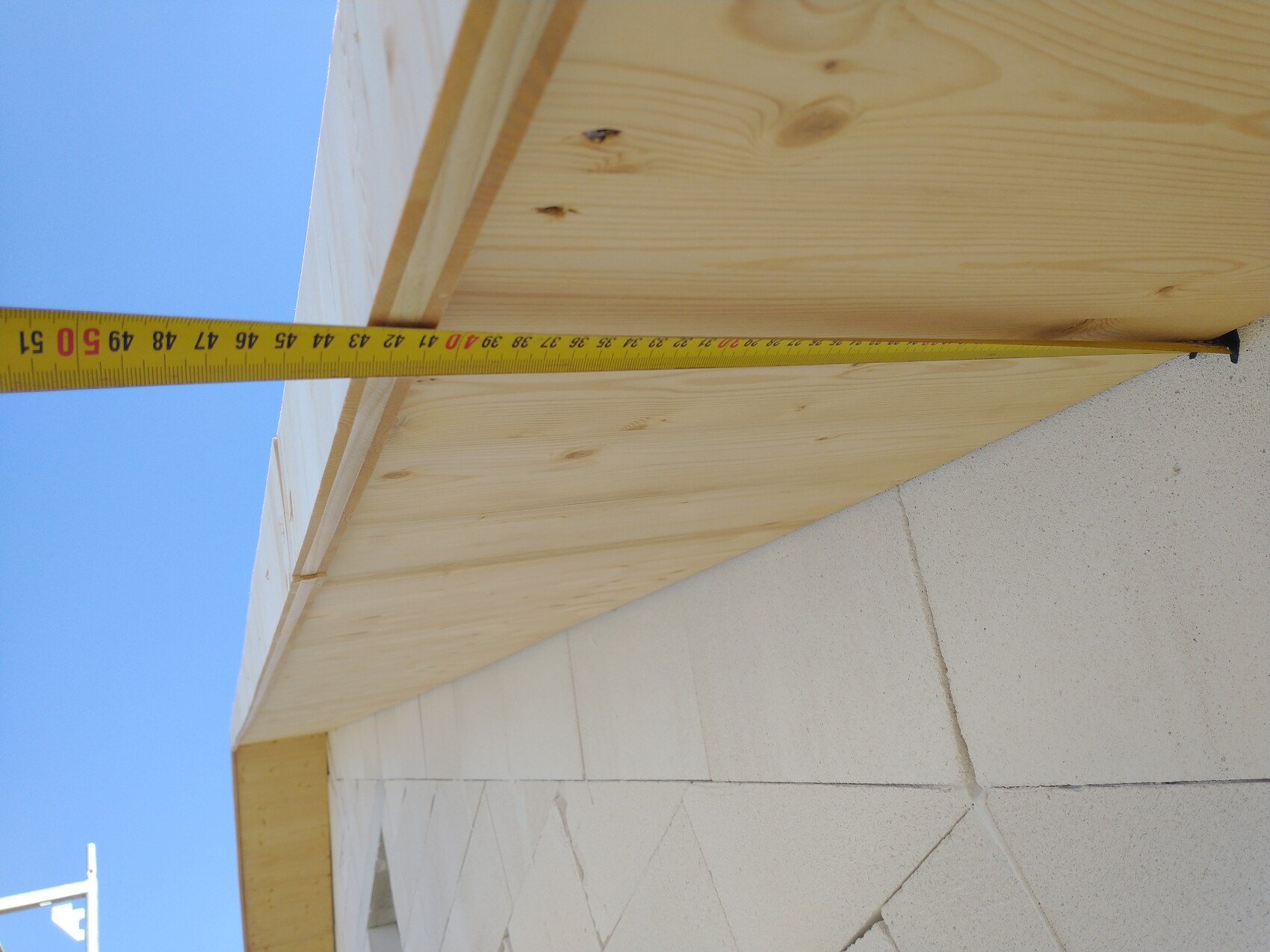 Measuring tape laid across wooden planks at a construction site, concrete wall underneath, blue sky.