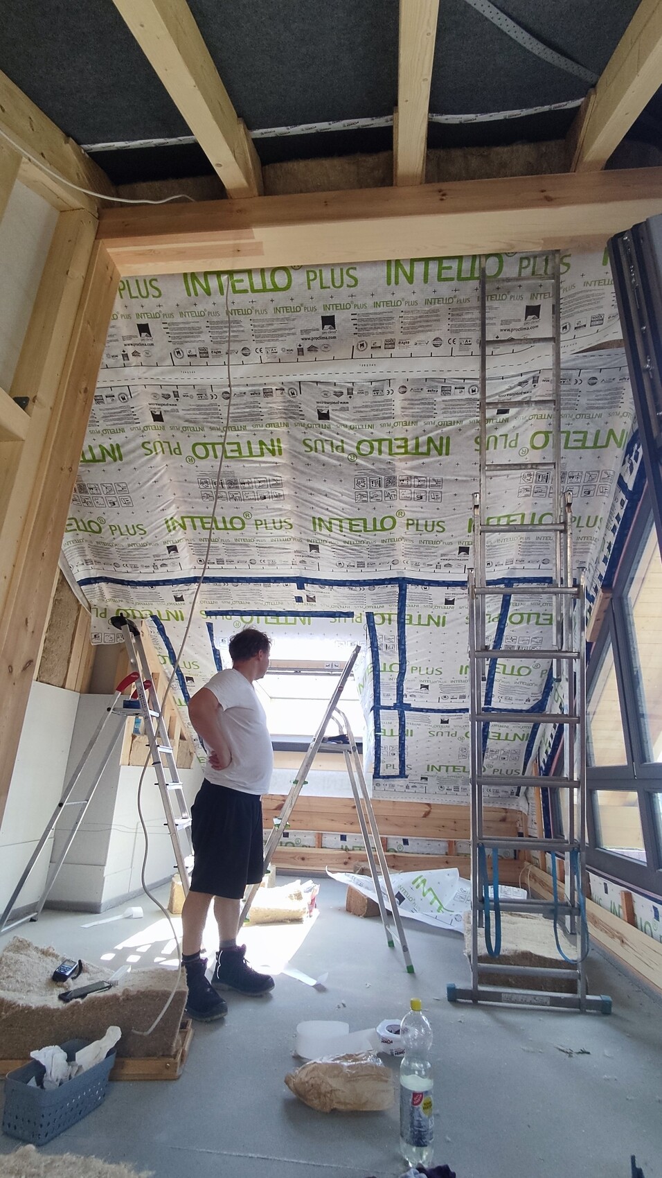 Man in construction room with ladder, INTELLO PLUS insulation on walls, building materials.