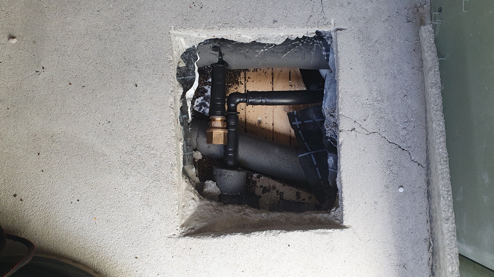 Exposed piping in the floor: black pipes, brass shutoff valve, concrete opening.