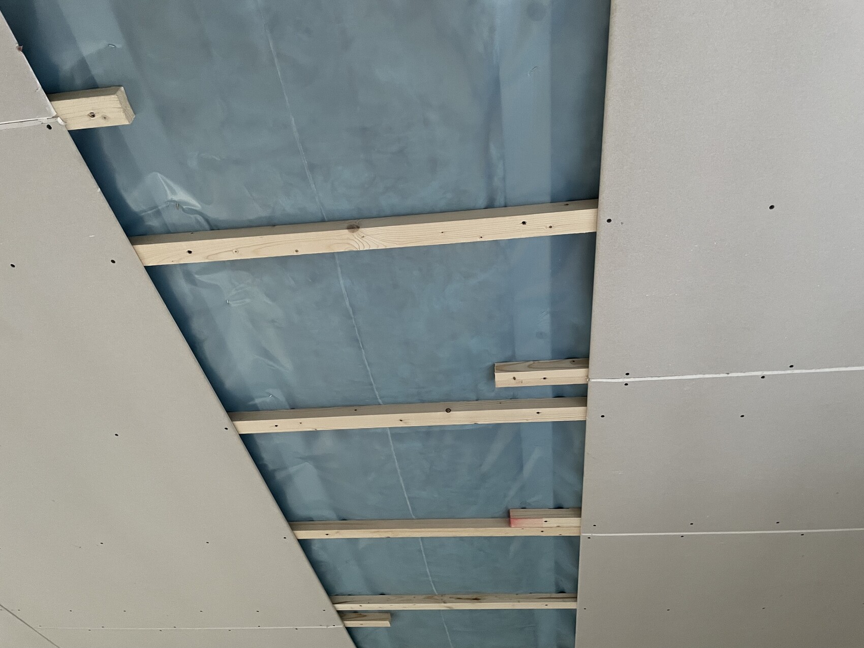 Ceiling substructure with wooden battens, blue moisture protection foil, and gypsum plasterboards