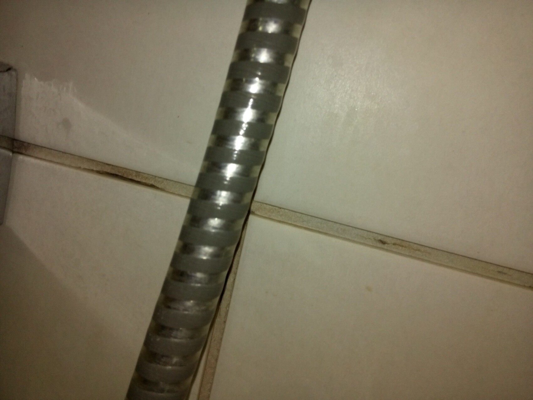 Close-up of a flexible metal conduit running over tiles