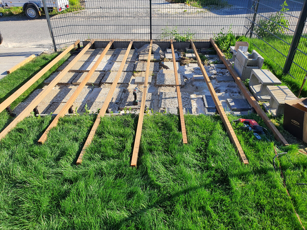 Wooden terrace frame being constructed in the garden on concrete foundations; grass in the foreground.