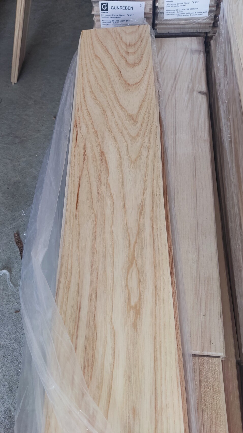 Long wooden plank with light grain, surrounded by other wooden boards in plastic wrap.