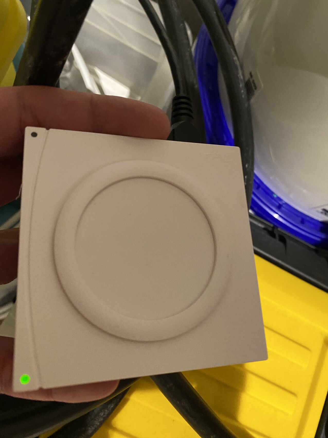 White square device with round recessed ring, green LED bottom left, cables in the background