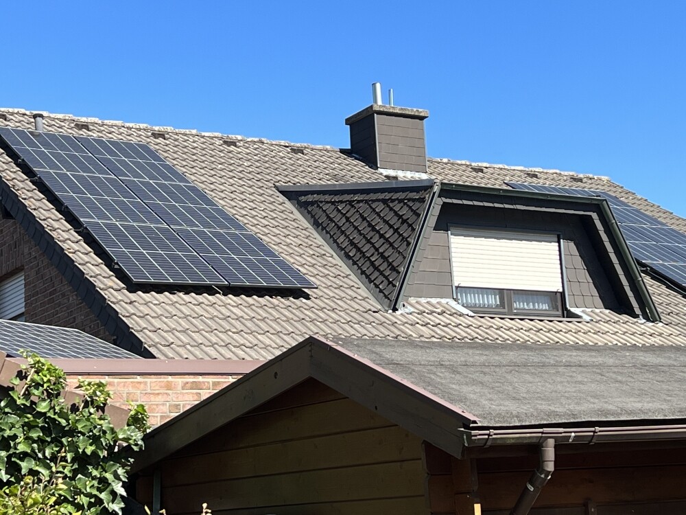 Dach eines Hauses mit Solarzellen auf beiden Seiten, Gaube mit Rollladen, blauer Himmel