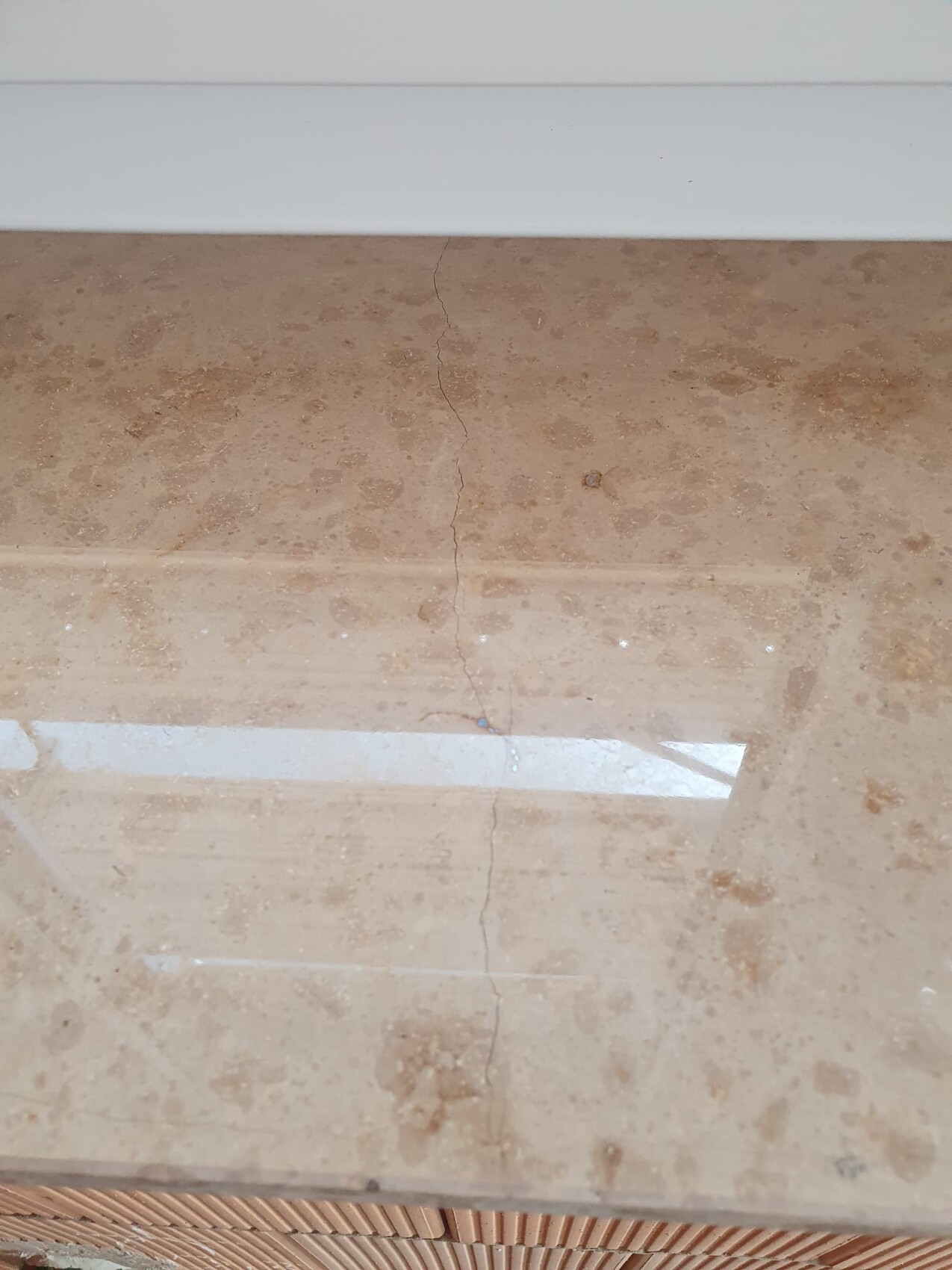 Beige stone worktop with visible hairline crack and stains, white wall above.