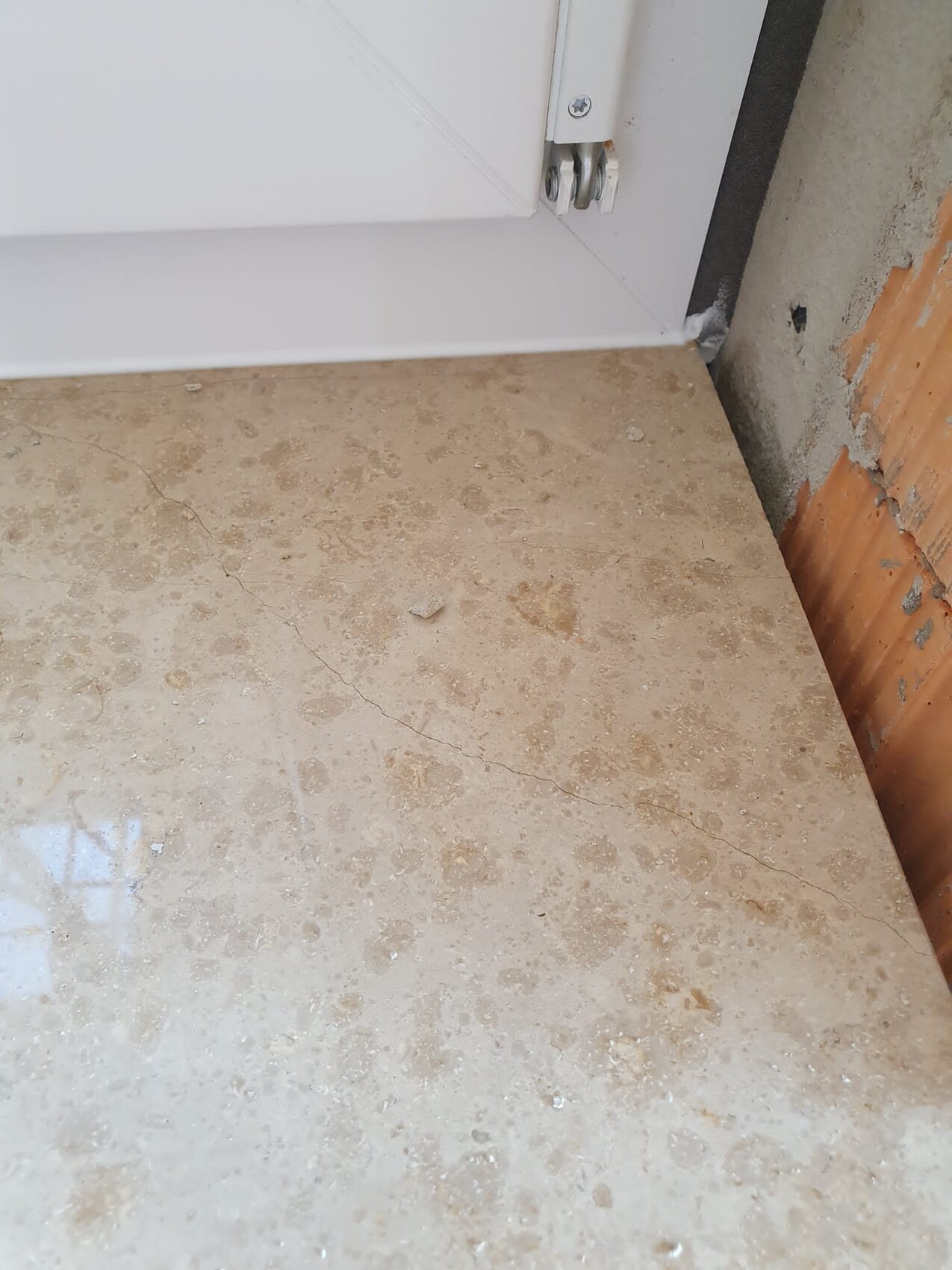 Underside of a white door with threshold, concrete floor with cracks, brick wall on right.