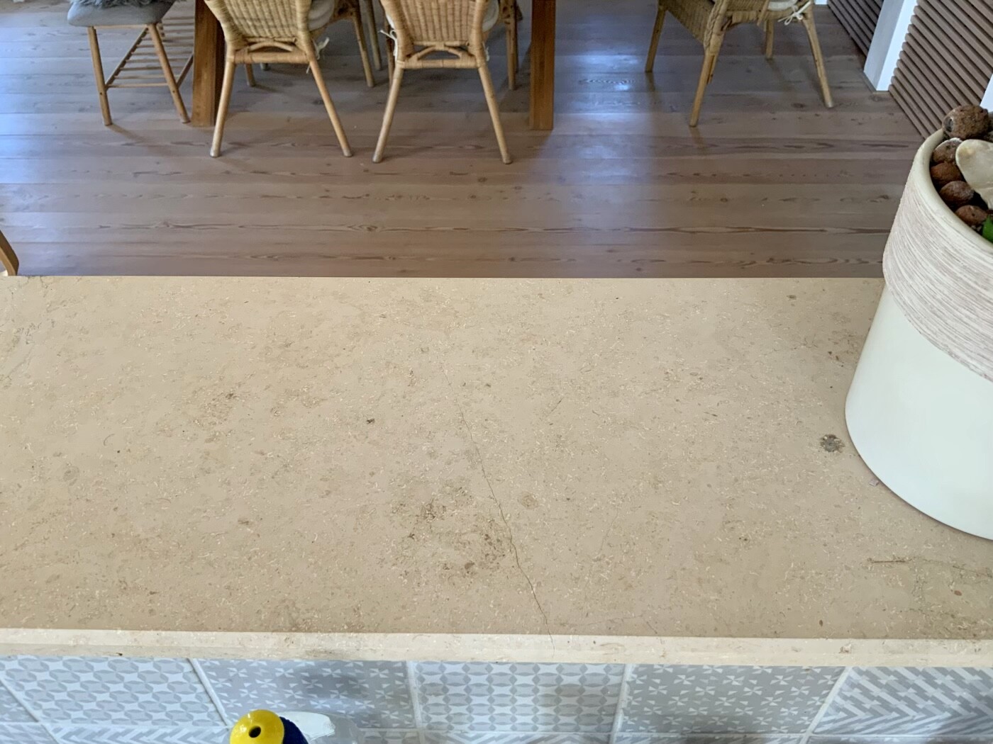Kitchen: View over countertop onto wooden floor and dining table with chairs, right side top potted plant.