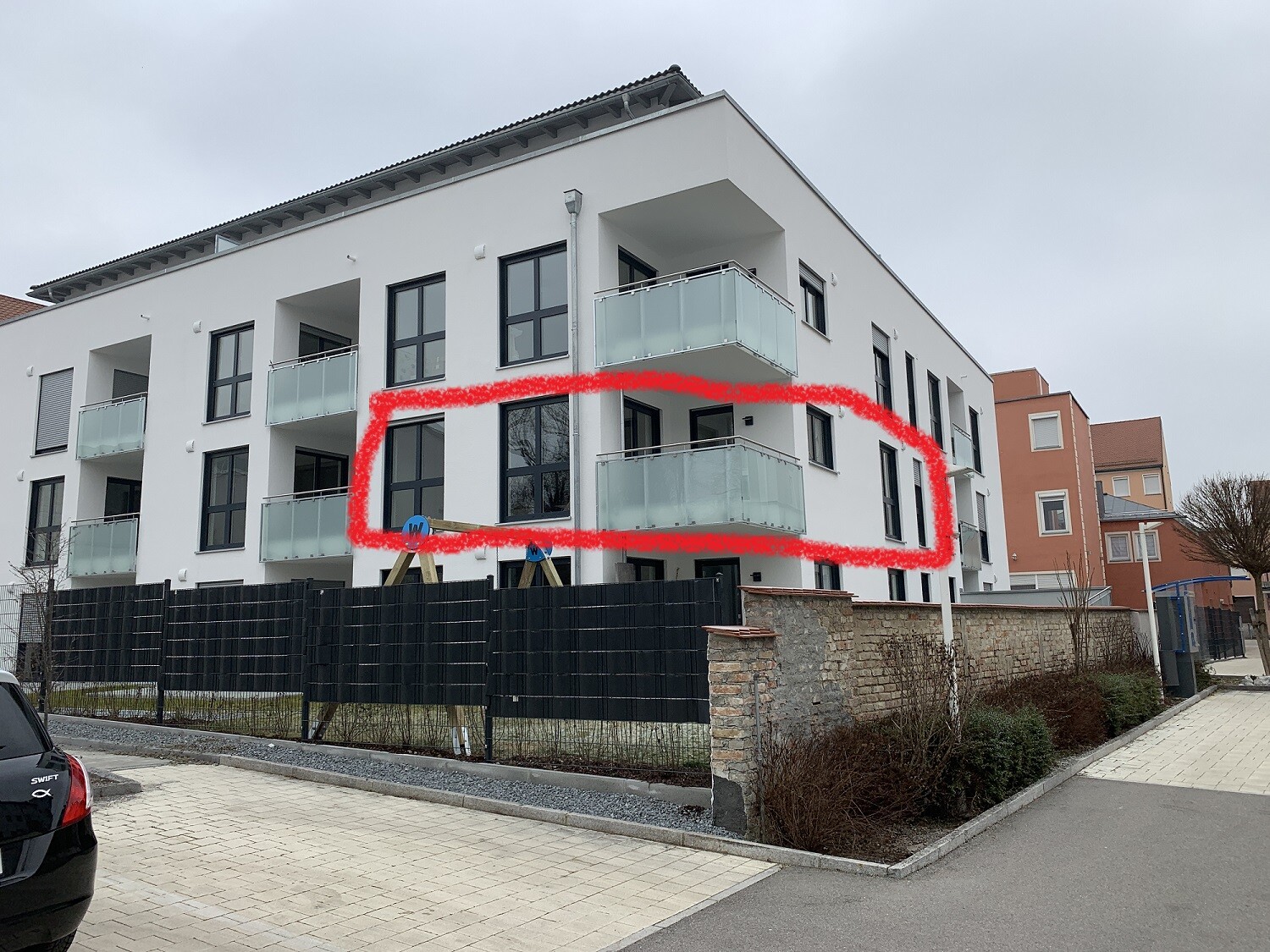 Modern white residential complex with glass balconies; red marking around the balconies in the middle section of the building.