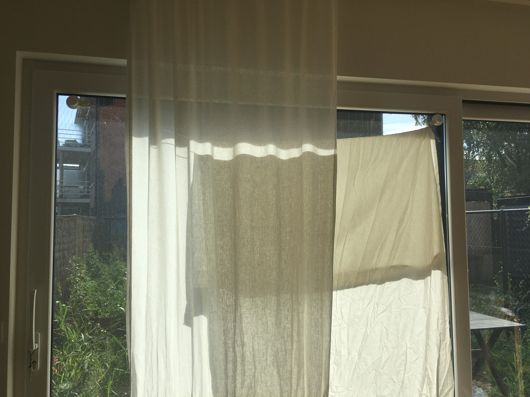 Interior with glass sliding door; sheer curtain, white cloth hanging outside on the line.