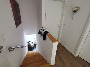 Wooden staircase in a bright stairwell with railing and door at the bottom.