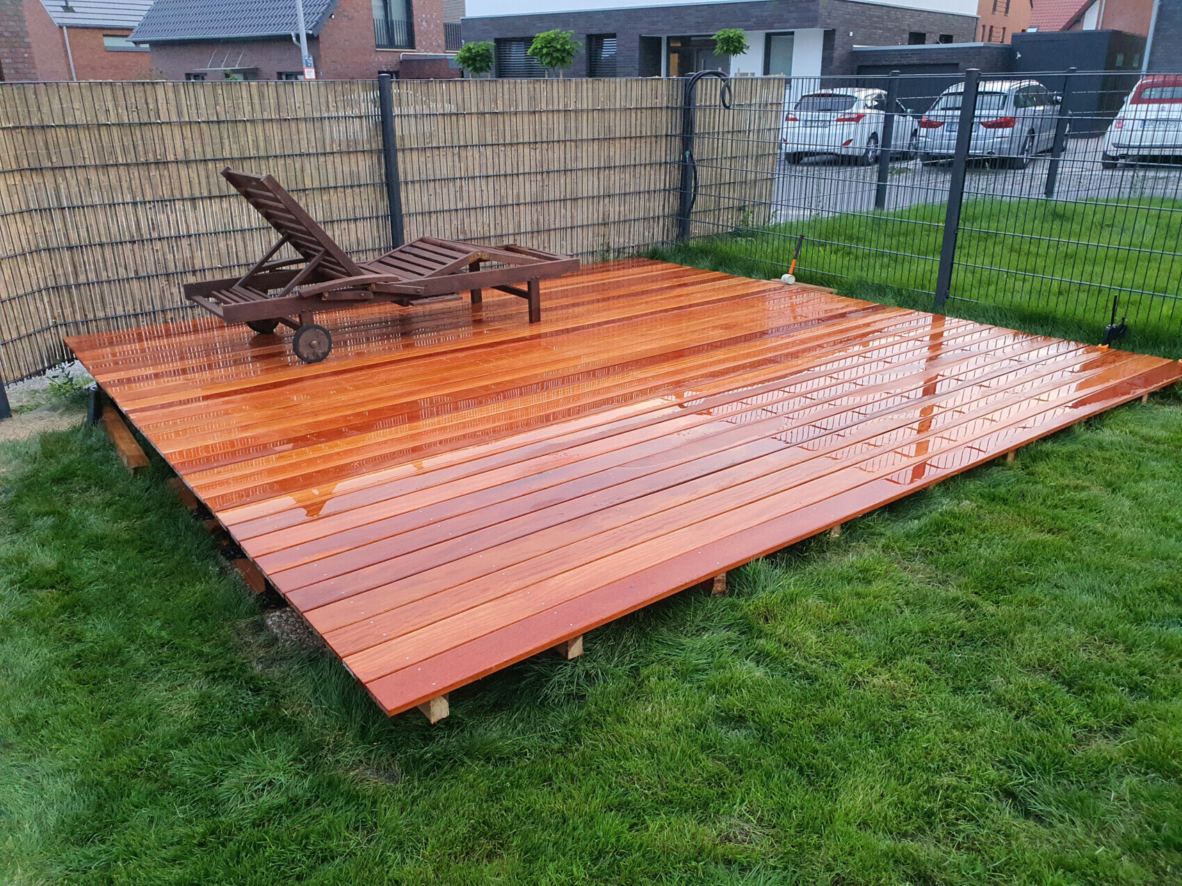Orangefarbene Holzdeckplatte im Garten mit Lounge-Stuhl, Zaun und Autos im Hintergrund